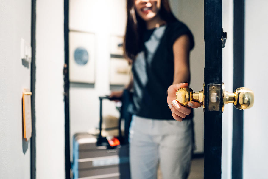 Cheerful young Asian female traveller opening the door entering the hotel room. She is carrying a suitcase and on vacation Photograph by D3sign