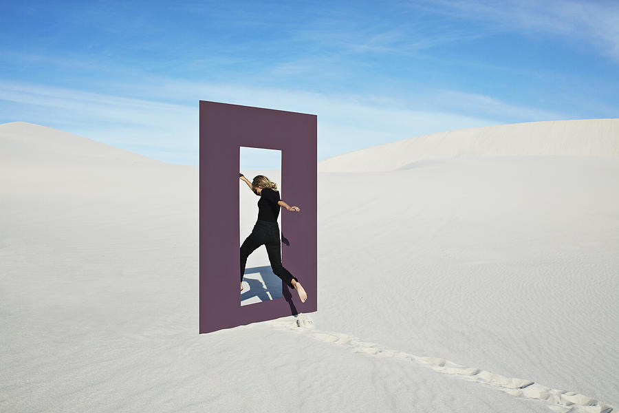 Cheerful young woman jumping through door frame at desert Photograph by Klaus Vedfelt
