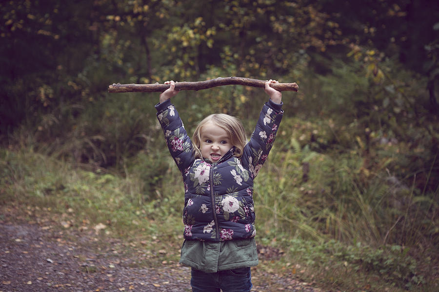 Child on a forest path, holding a big stick above her head Photograph by Elva Etienne