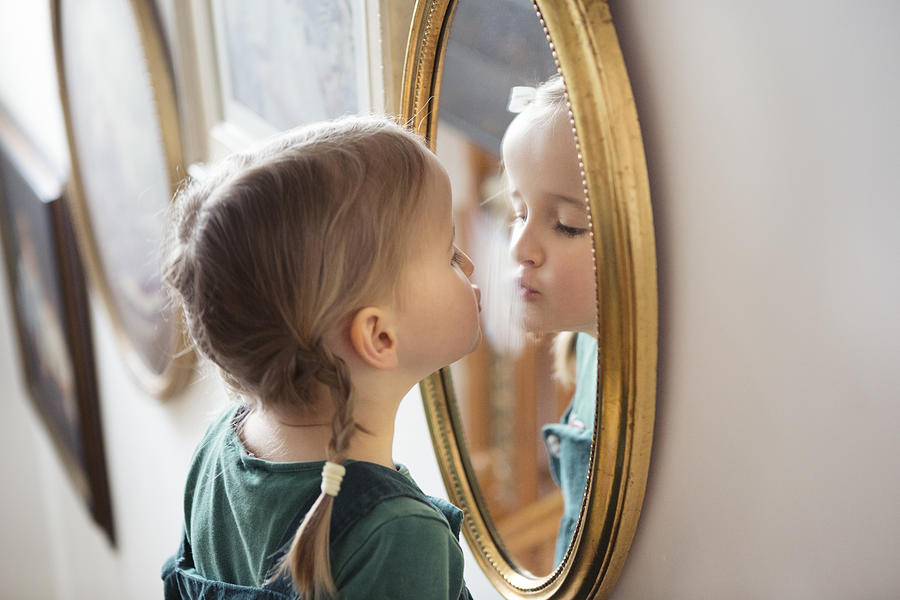 Child puckering up at her own reflection in a mirror, whilst steaming the glass with her breath Photograph by Elva Etienne