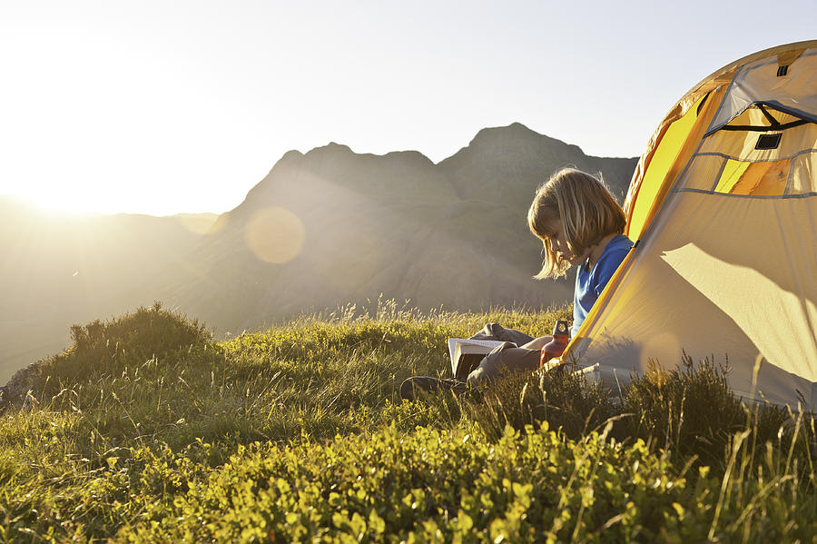 Child reading in idyllic summer sunset light camping in mountains Photograph by fotoVoyager