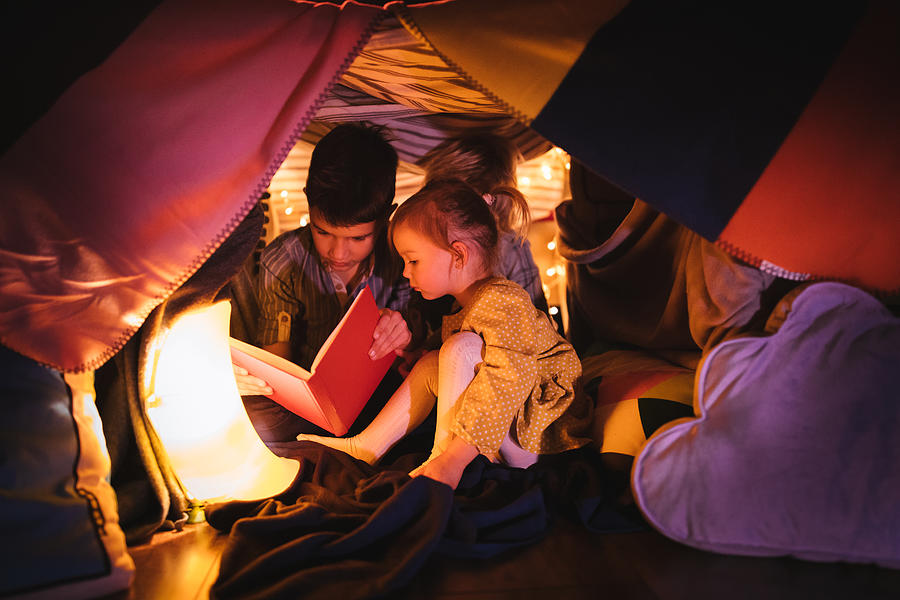Children reading a story in blanket fort at night Photograph by Wundervisuals