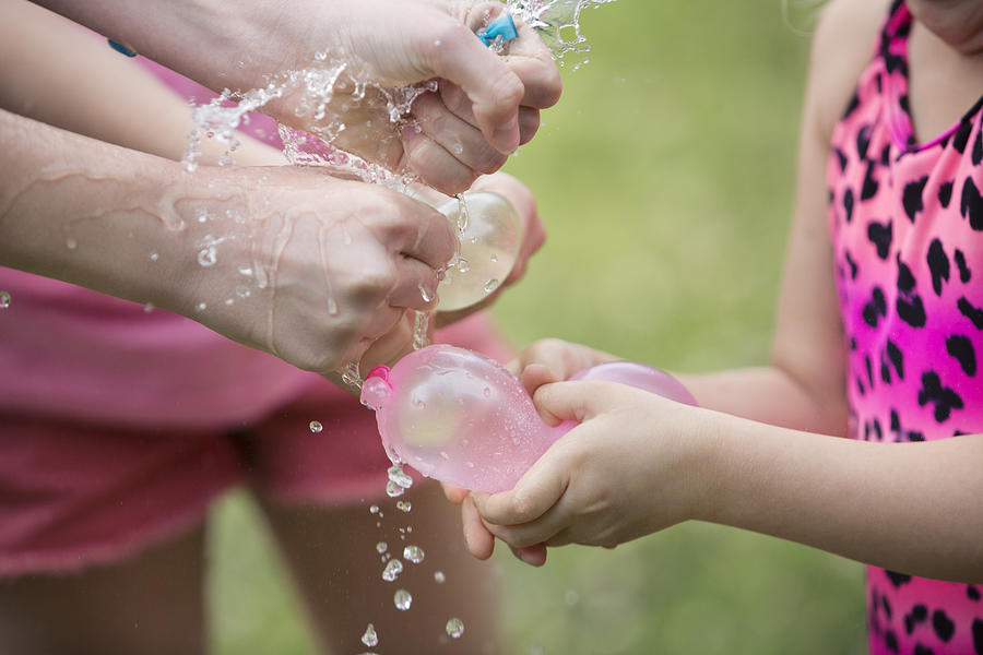 Children squeezing and bursting water balloons Photograph by Elva Etienne