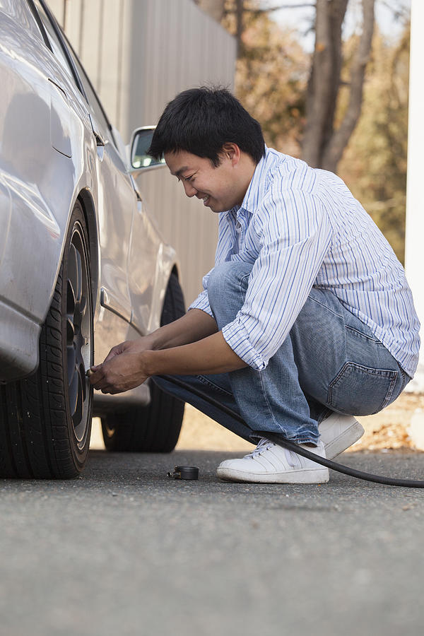 Chinese man putting air in his car tires Photograph by Mark Hunt