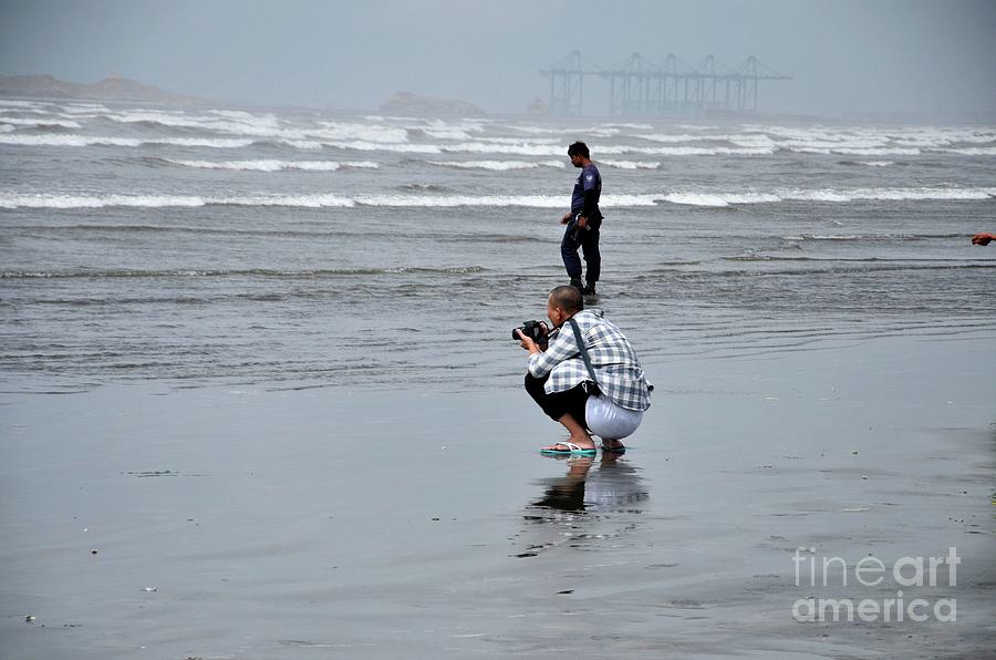 Chinese man squats with camera taking photo at Sea View beach water Karachi Pakistan Photograph by Imran Ahmed
