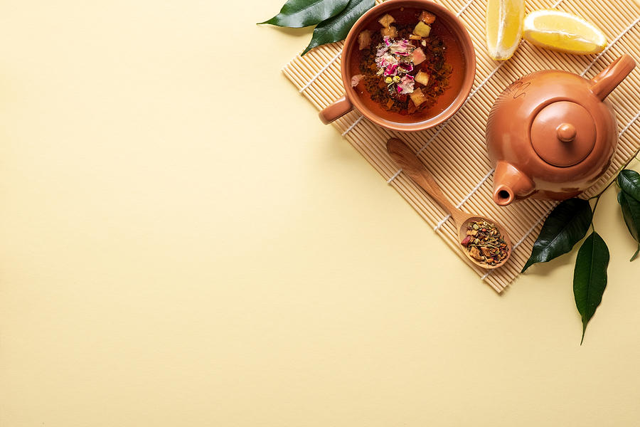 Chinese tea ceremony. Ceramic teapot, teacup, green leaves, wooden spoon with dried tea on bamboo mat on yellow background. Top view Photograph by Photoguns