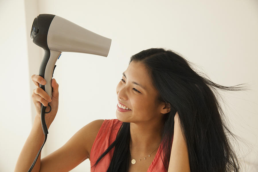 Chinese woman blow drying her hair Photograph by JGI/Jamie Grill