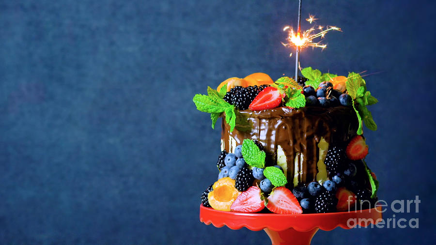 Chocolate drip cake decorated with fresh fruit and berries with copy space. Photograph by Milleflore Images