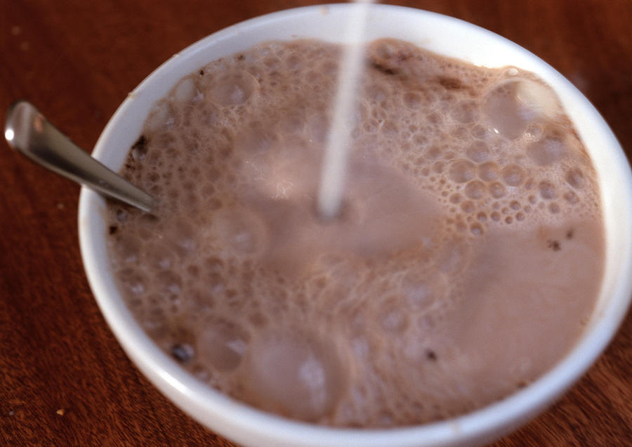 Chocolate milk in bowl, with spoon, liquid being poured into bowl, blurred Photograph by Isabelle Rozenbaum