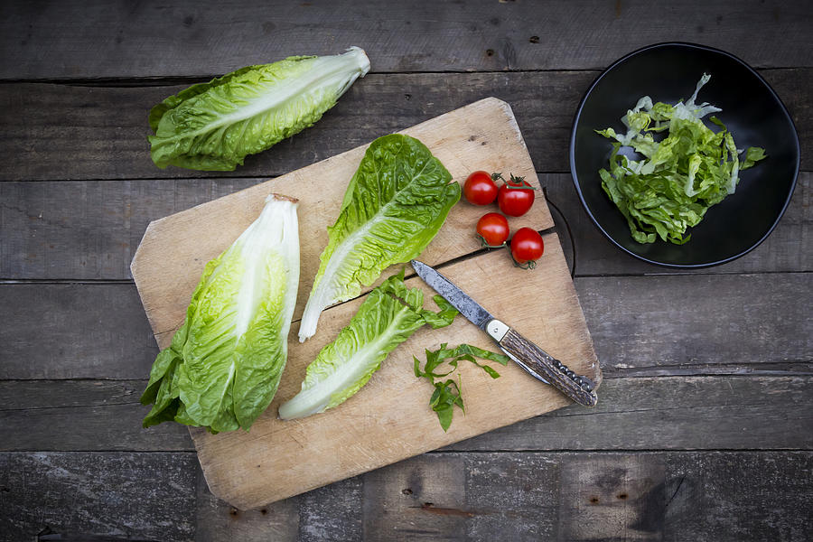 Chopped and whole romaine lettuce, pocket knife and tomatoes on wooden board Photograph by Westend61