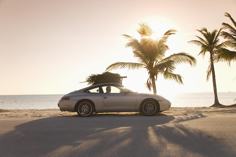 Christmas tree on top of car on beach, side view Photograph by Buena Vista Images