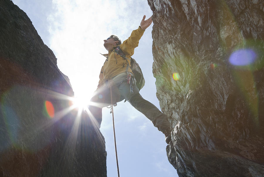 Climber stands above rock crack, arms outstretched Photograph by Ascent Xmedia