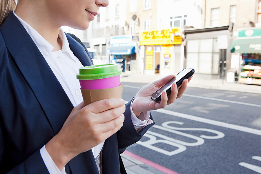 Close of businesswoman on street with coffee and smart phone Photograph by Image Source