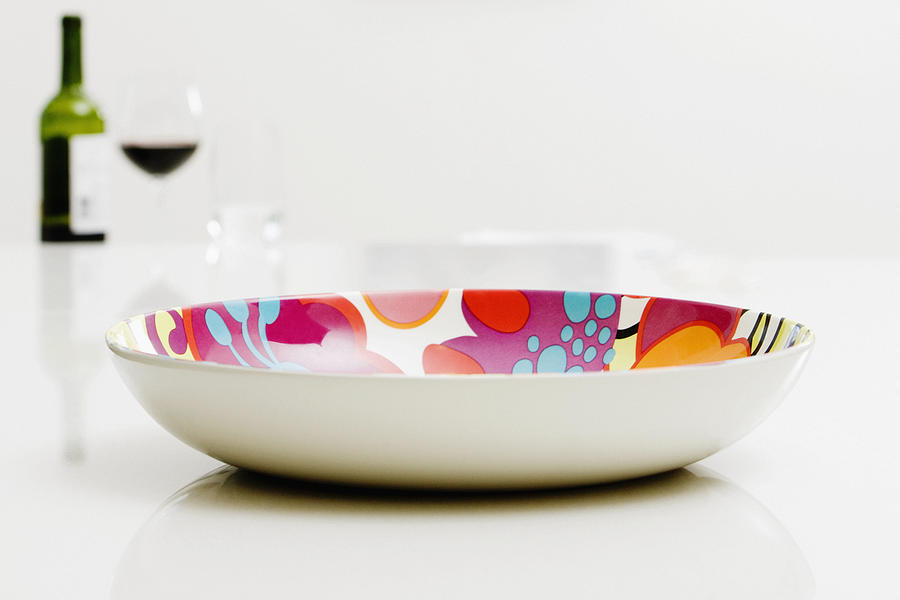 Close-up of a bowl with a bottle of red wine in the background Photograph by Glowimages