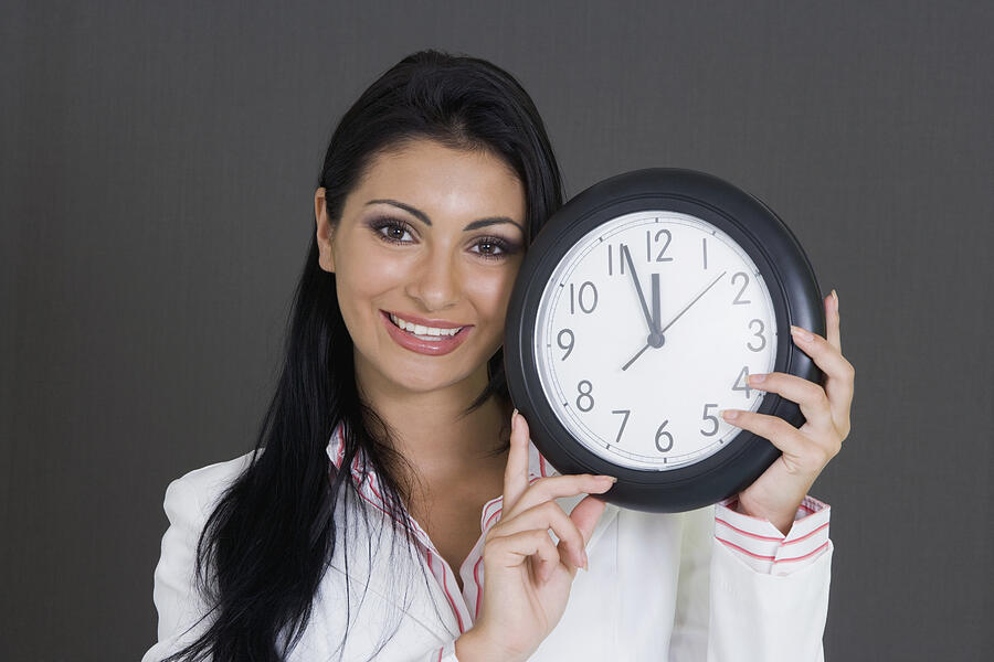 Close-up of a businesswoman holding a clock and smiling Photograph by Glowimages