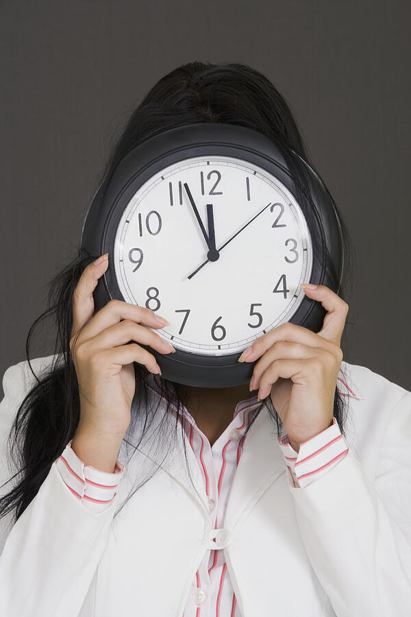 Close-up of a businesswoman holding a clock in front of her face Photograph by Glowimages