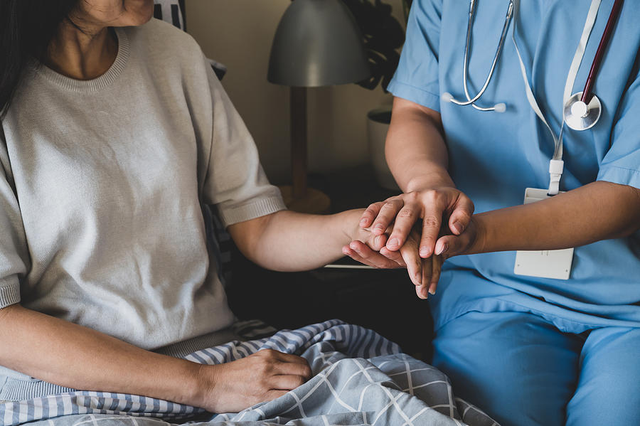 Close-up of a female nurse holding hands for reassuring her female patient on bed. Photograph by Goc Close-up of a female nurse holding hands for reassuring her female patient on bed. Photograph by Goc