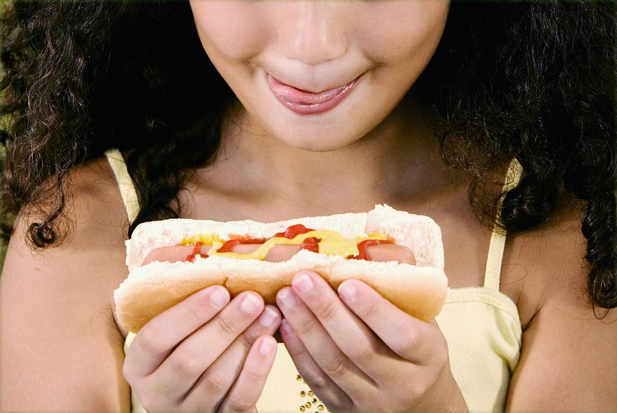 Close-up of a girl holding a hot dog and sticking her tongue out Photograph by Glowimages