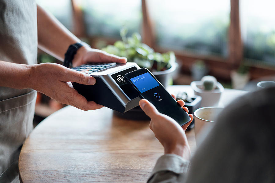 Close up of a males hand paying bill with credit card contactless payment on smartphone in a cafe, scanning on a card machine. Electronic payment. Banking and technology Photograph by AsiaVision