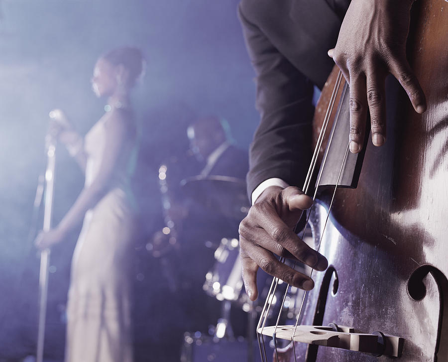 Close-up of a Man Plucking a Double Bass on Stage in a Nightclub and a Female Singer and Saxophonist Standing in the Background Photograph by Nick White