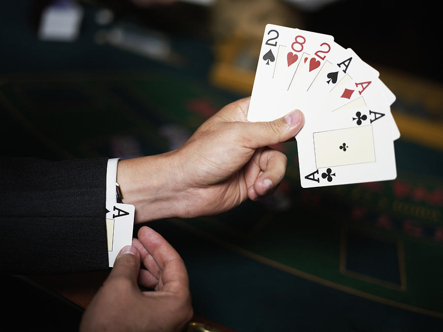 Close-up of a persons hand holding playing cards and hiding an ace in his cuff Photograph by Glowimages