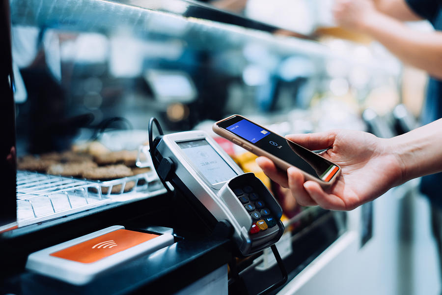 Close up of a womans hand paying with her smartphone in a cafe, scan and pay a bill on a card machine making a quick and easy contactless payment. NFC technology, tap and go concept Photograph by D3sign