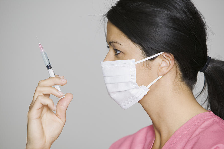 Close Up Of A Young Adult Female Nurse In A Mask As She Holds Up A Syringe Photograph by Photodisc