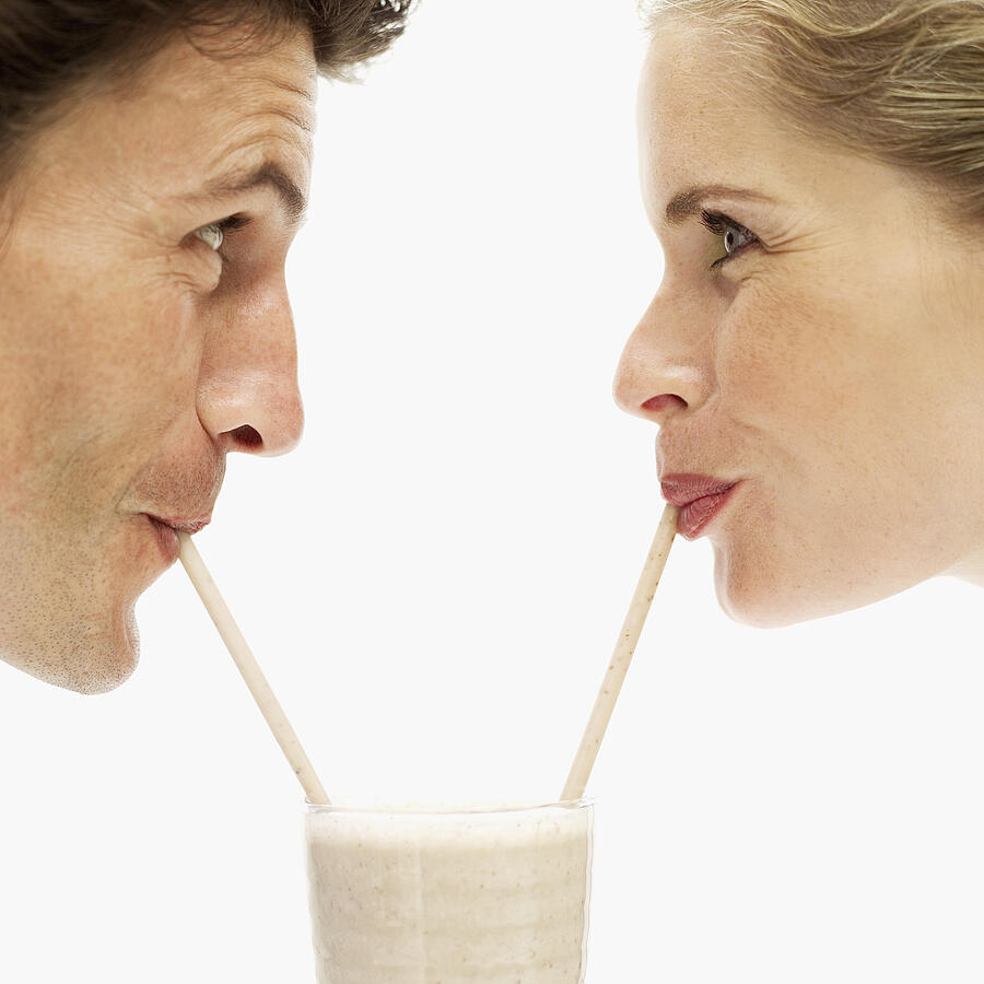 Close-up of a young couple drinking a milkshake from a glass with straws Photograph by Stockbyte