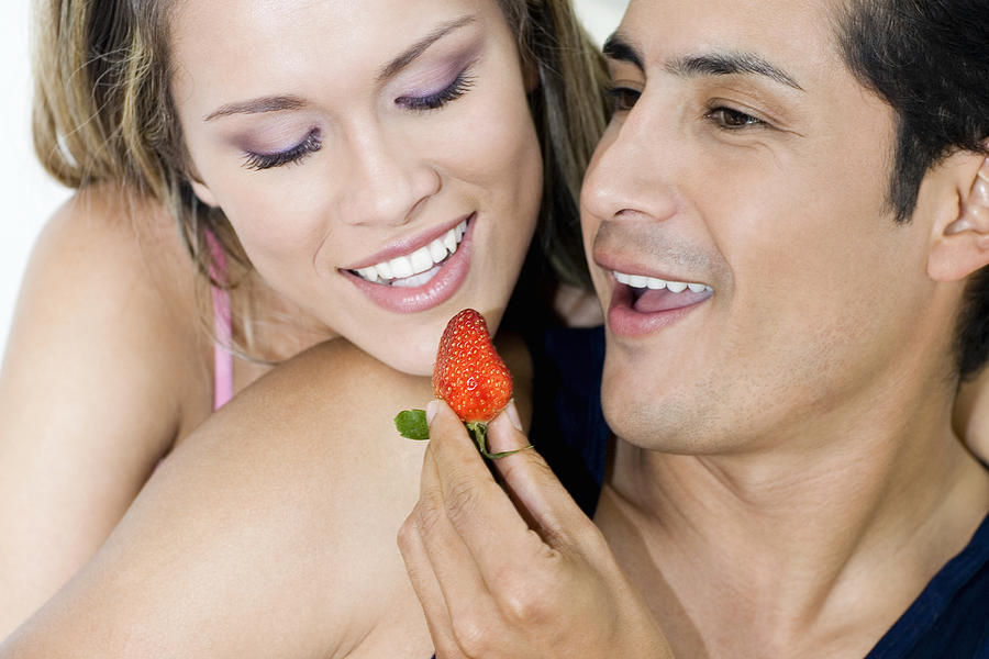 Close-up of a young man feeding a strawberry to a young woman Photograph by Glowimages