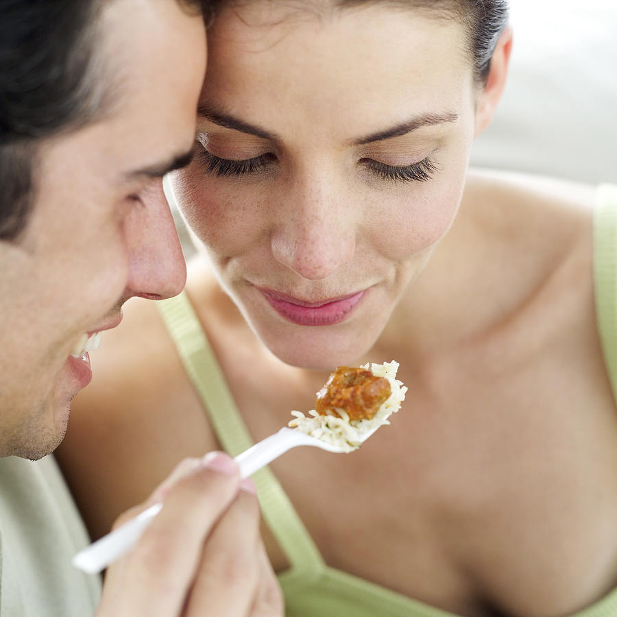 Close-up Of A Young Man Feeding A Young Woman With A Plastic Fork Photograph by Stockbyte