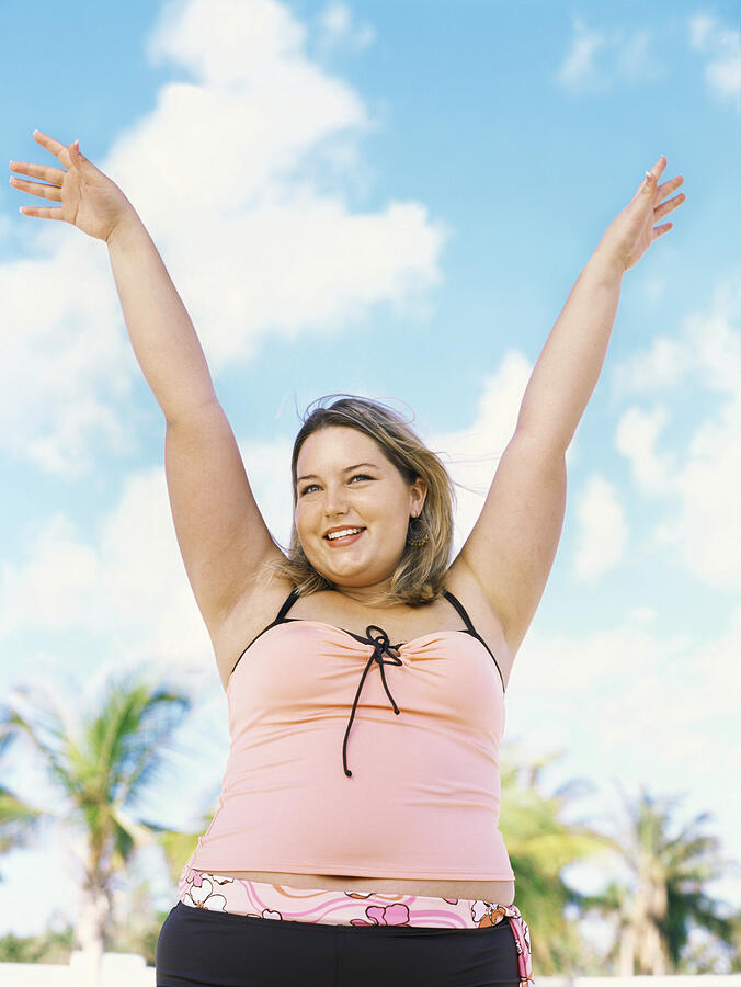Close-up of a young overweight woman standing on the beach with her arms raised Photograph by George Doyle