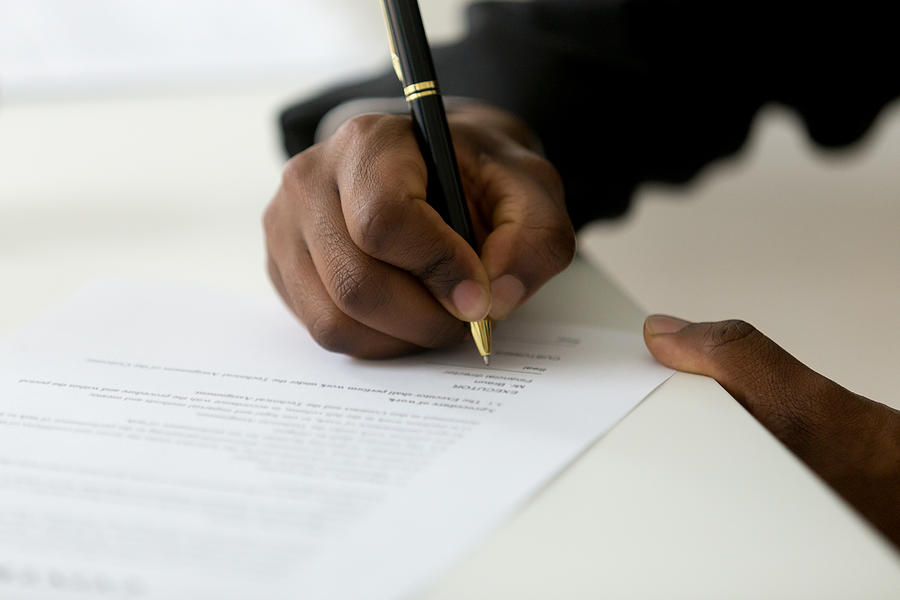 Close up of black worker signing legal documentation Photograph by Fizkes