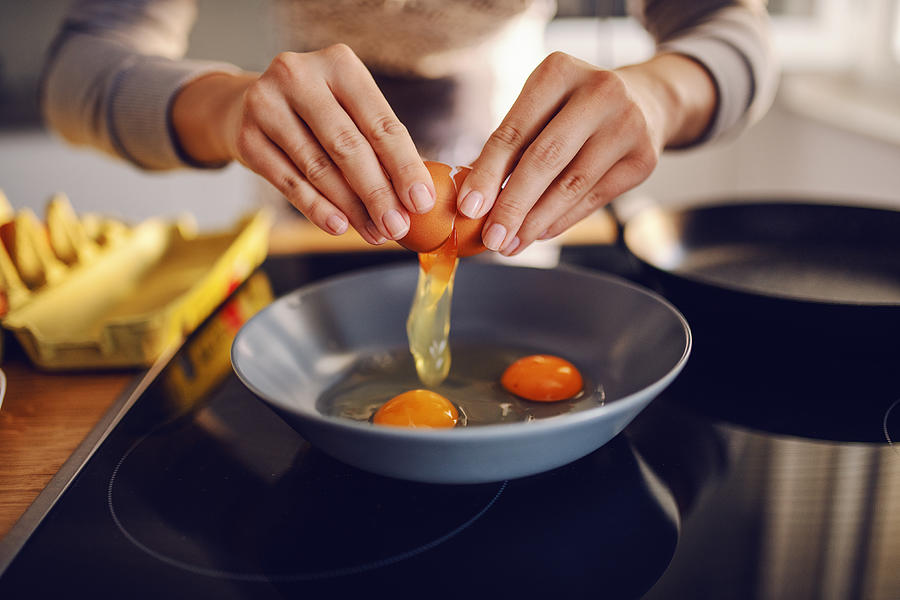 Close up of caucasian woman breaking egg and making sunny side up eggs. Domestic kitchen interior. Breakfast preparation. Photograph by Dusanpetkovic