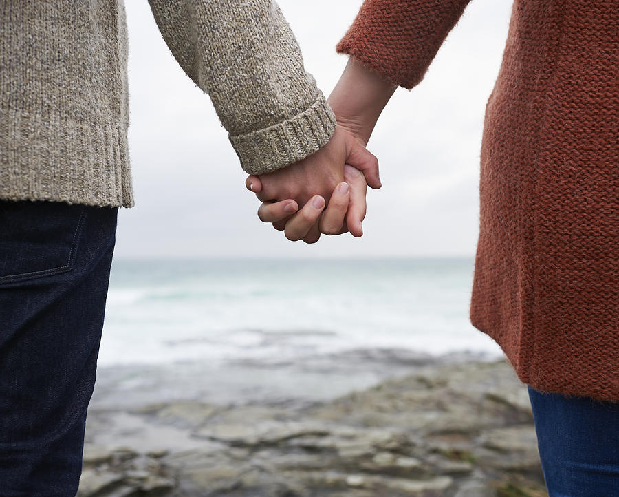 Close up of couple holding hands on coastline. Photograph by Dougal Waters