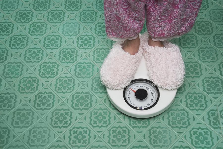 Close up of feet in slippers on bathroom scale Photograph by Terry Vine