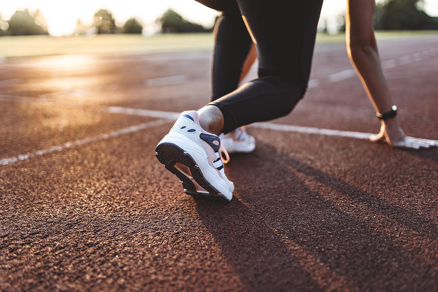 Close up of female athlete getting ready to start running on track . Focus on sneakers Photograph by Ljubaphoto