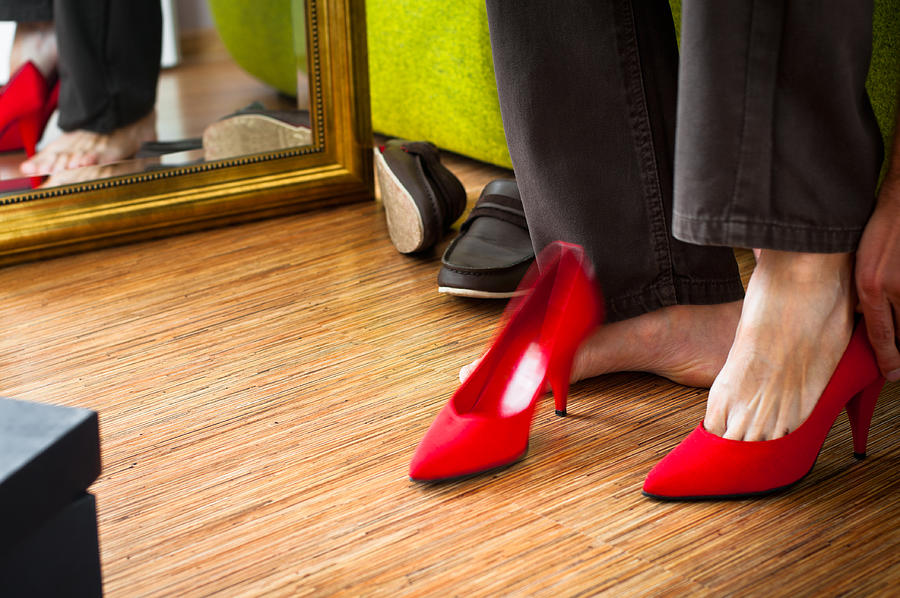Close-up of man trying on red womans high-heels, wardrobe interior Photograph by Domin_domin