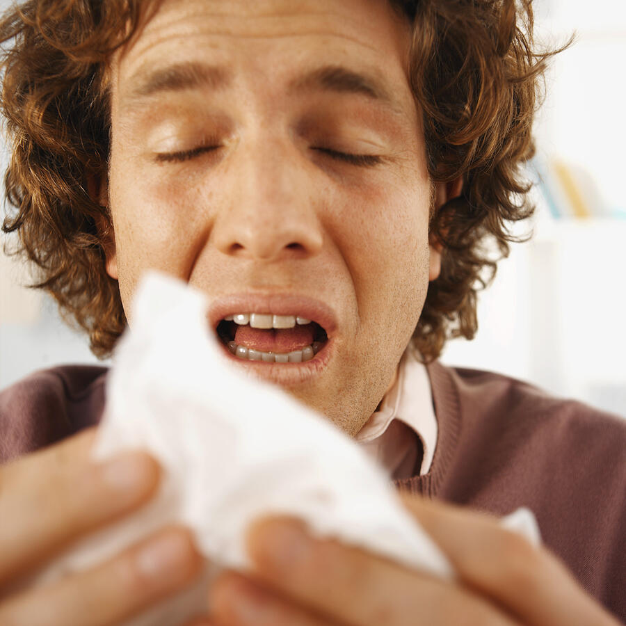 Close-up of mid adult man sneezing into tissue Photograph by Stockbyte