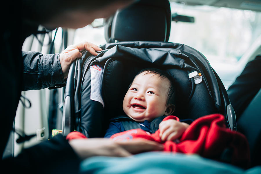 Close up of mother taking care of cute smiling baby on car seat in car Photograph by D3sign