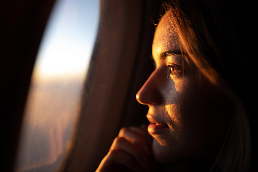 Close up of pensive woman looking at sunset through airplane window. Photograph by Skynesher