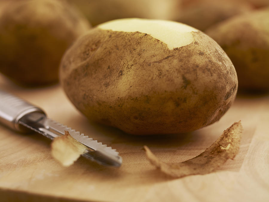 Close up of potato and peeler on cutting board Photograph by Adam Gault