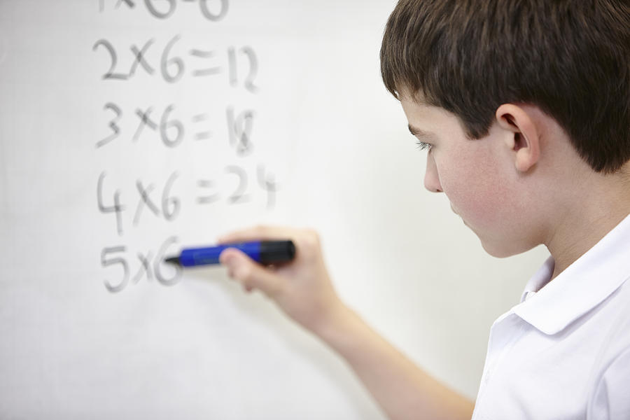 Close up of schoolboy doing multiplication on white board Photograph by Phil Boorman