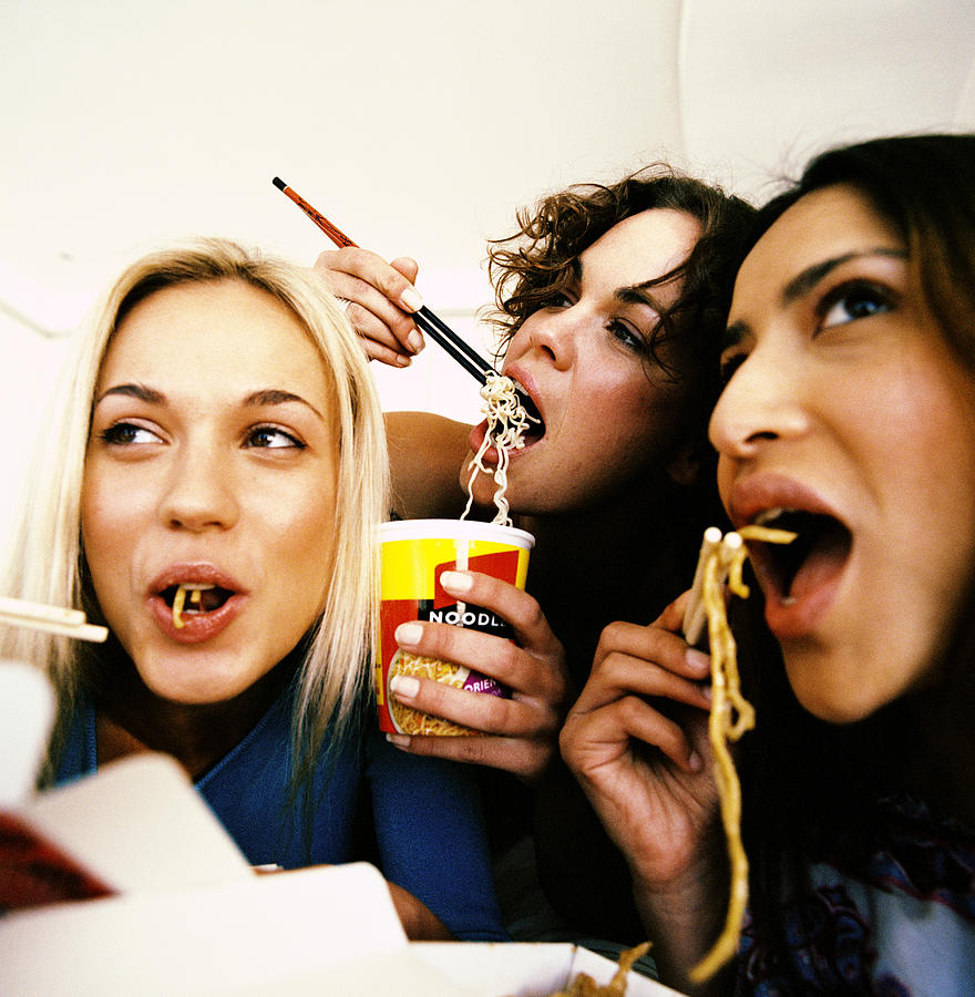 Close-up of three young women eating instant noodles Photograph by Stockbyte