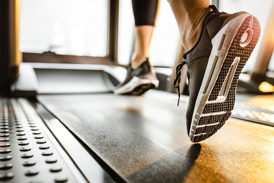 Close up of unrecognizable athlete running on a treadmill in a gym. Photograph by Skynesher