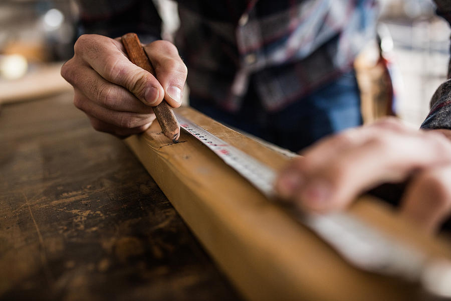 Close up of unrecognizable carpenter marking measurements on a piece of wood. Photograph by Skynesher