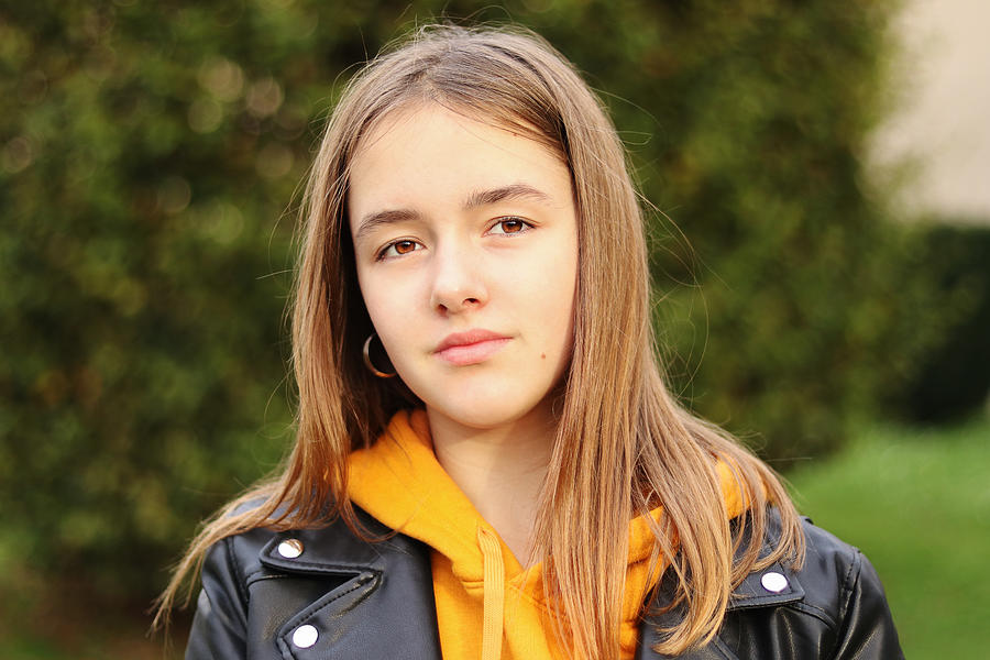 Close up portrait of beautiful teenager girl with brown eyes in hoodie and biker jacket outdoors looking at camera. Natural beauty of youth, no makeup. Photograph by Tetiana Soares