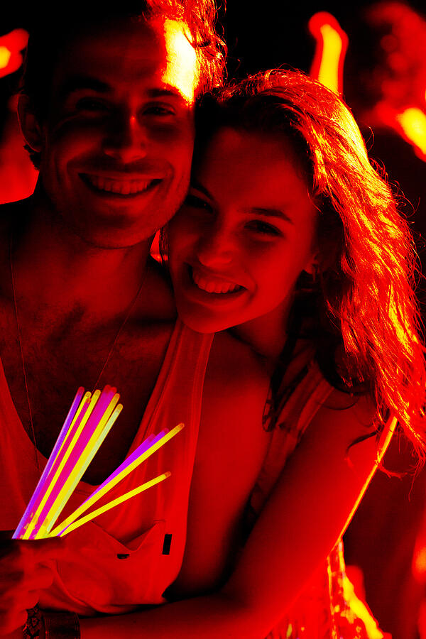 Close up portrait of happy couple with glow sticks at music festival Photograph by Caia Image