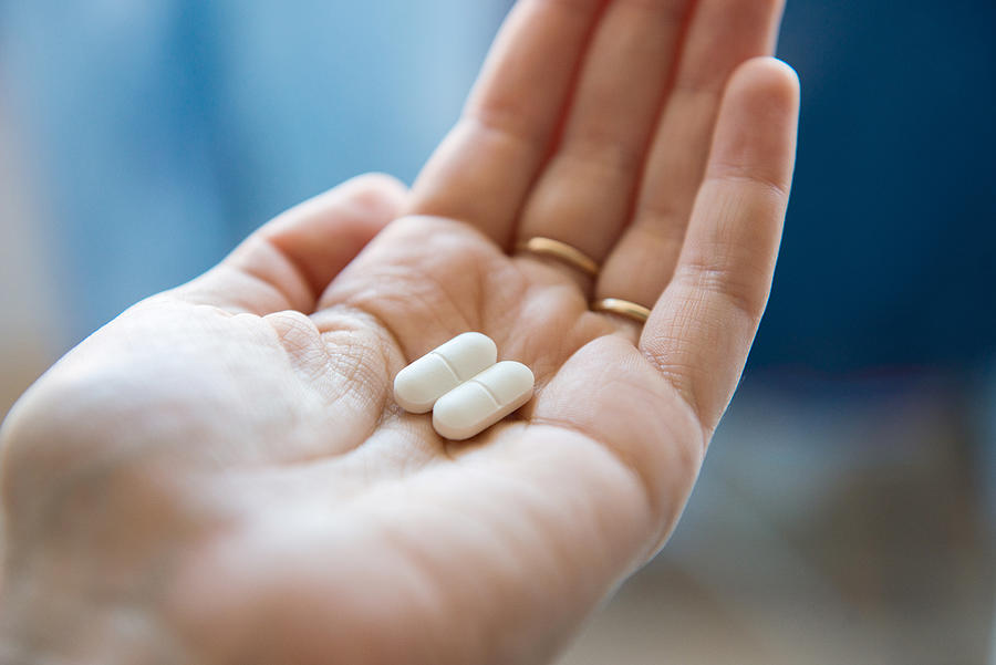 Close-up view of a hand holding two white pills in the palm above a blurry background, painkiller Photograph by Oleksandra Troian