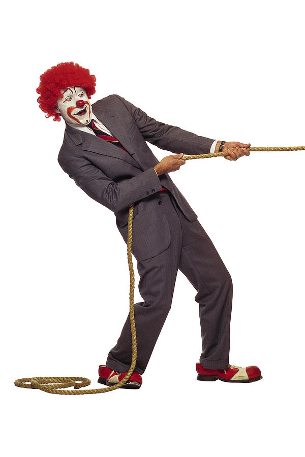 Clown in business suit tugging on rope Photograph by Comstock