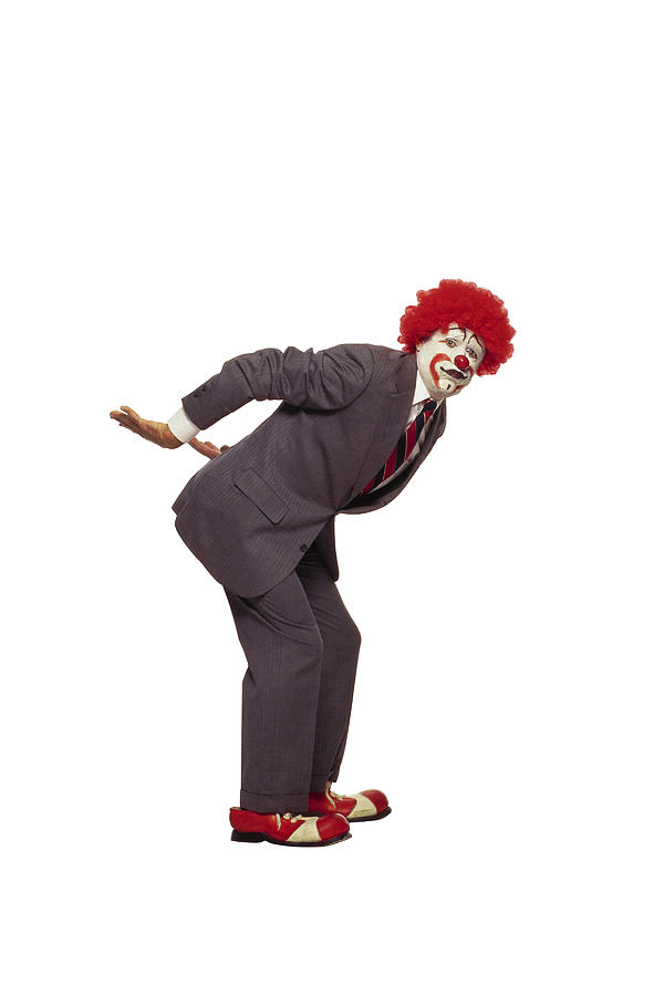 Clown in business suit with arms behind back lifting Photograph by Comstock